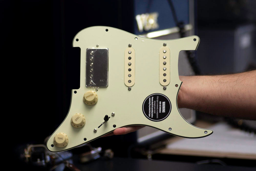An Obsidianwire HSS loaded pickguard with aged white hardware, a nickel covered humbucker and mint green pickguard. The pickguard is hand held with a blurred background.