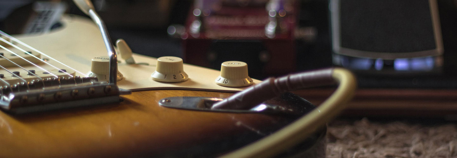 A wide banner image showing the tone and volume controls f a Fender stratocaster. The knobs are aged white, while the body is a traditional three tone sunburst.