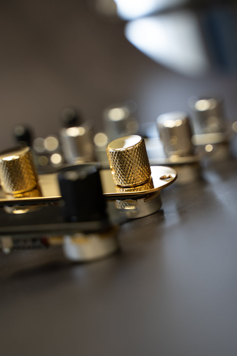 A row of four different colors of loaded telecaster control plate. Only the gold loaded control plate is in focus, while the black, nickel and chrome loaded control plates are out of focus.