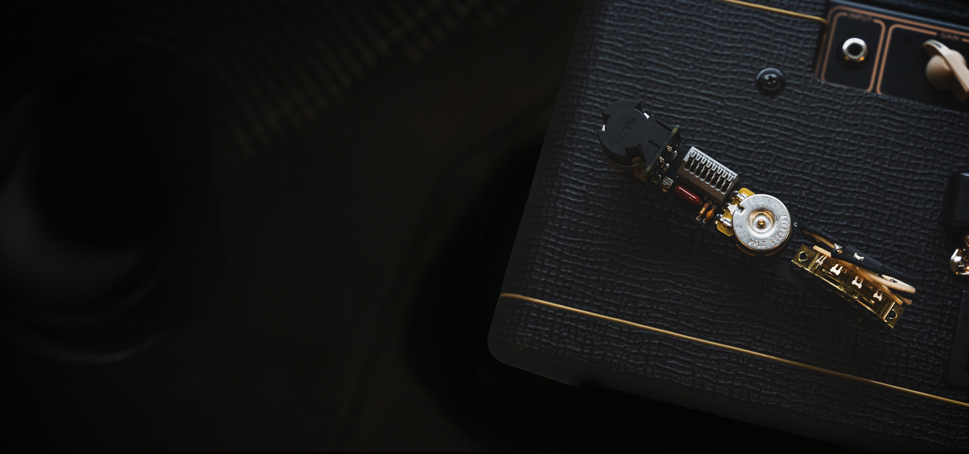 An obsidianwire solderless wiring harness set on top of a black Vox AC10 guitar amp. The background is black to contrast the wiring harness